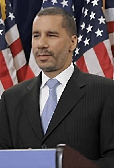 A man in suit and tie standing next to an american flag.