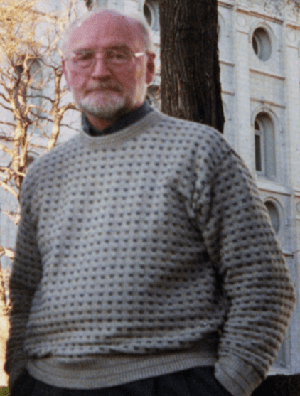 A man in grey sweater standing next to tree.