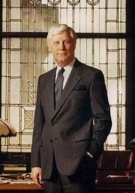 A man in suit and tie standing next to desk.